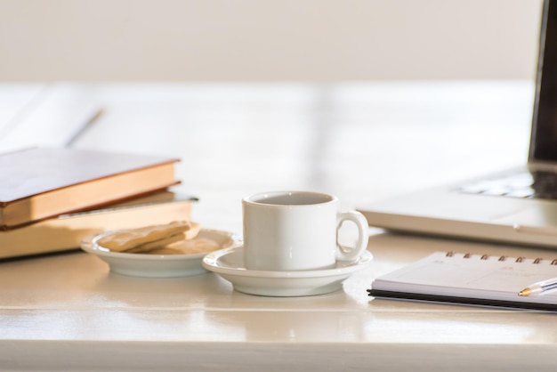 Libri impilati con una tazzina di caffè, un'agenda xA e un computer portatile che pianifica la mattinata