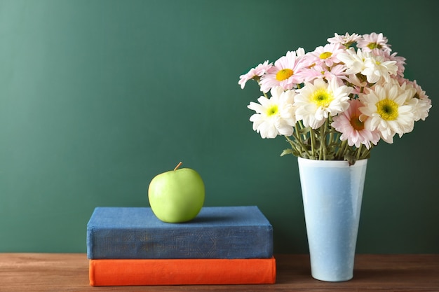 Libri, mela e fiori su tavola di legno