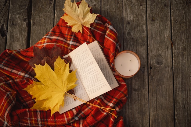 Libro aperto con candela e bouquet di foglie autunnali con un plaid su uno sfondo di legno