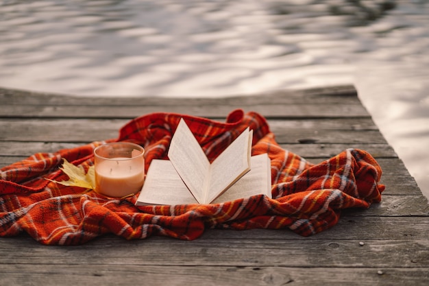 Libro aperto con candela e bouquet di foglie autunnali con un plaid su uno sfondo di legno