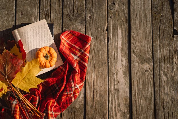 Libro aperto con un mazzo di zucca arancione di foglie autunnali con un plaid su uno sfondo di legno