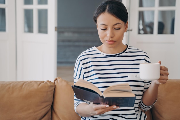 Libro bestseller di lettura del topo di biblioteca femminile che si rilassa con una tazza di caffè sul divano di casa Hobby dell'istruzione