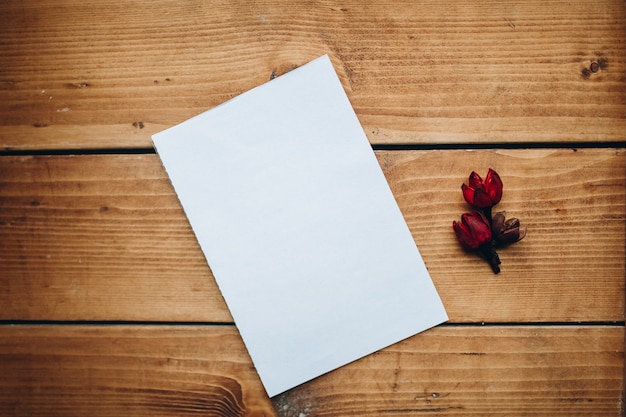 Libro bianco in bianco con fiore secco su una scrivania in legno.