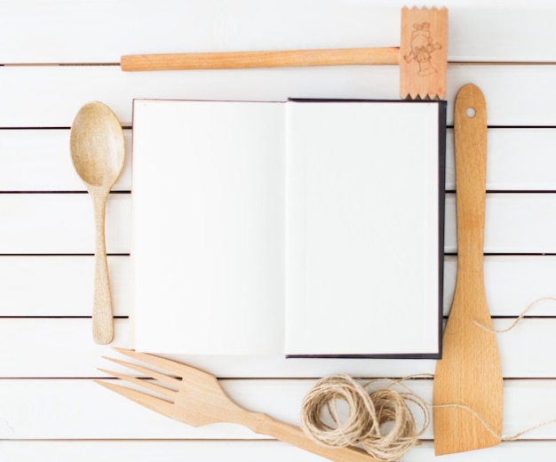 Libro bianco per ricetta con utensili da cucina su tavola di legno, vista dall'alto