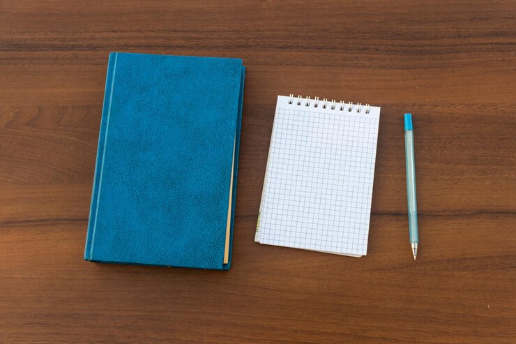 Foto libro chiuso, blocco note e penna su fondo in legno