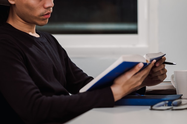 Libro di lettura del giovane allo scrittorio del lavoro a tarda notte, conoscenza e concetto di apprendimento