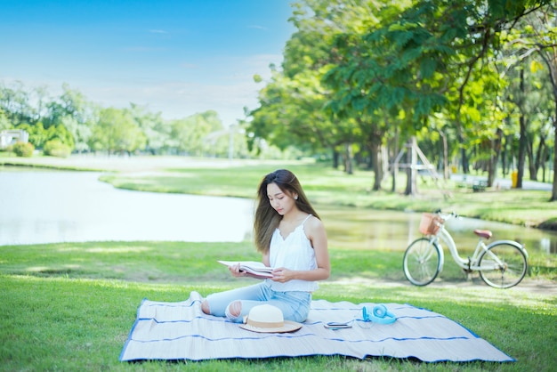 Libro di lettura della donna asiatica da solo nel parco il giorno di primavera. Relax e svago. Attività all'aperto e stile di vita in vacanza.