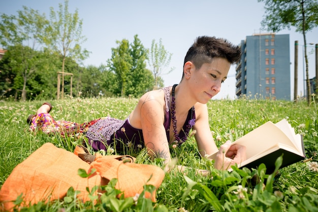 libro di lettura della donna dei bei capelli corti dei pantaloni a vita bassa nel parco