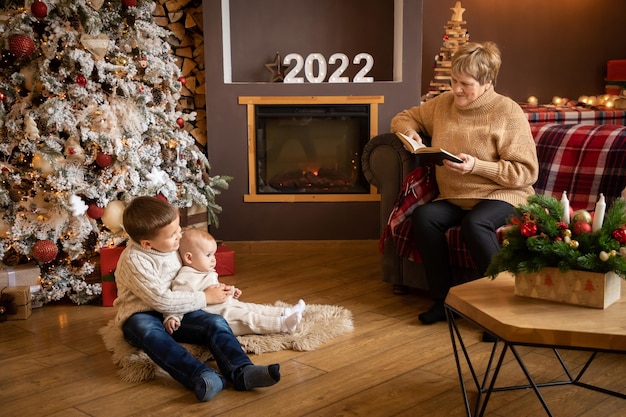 Libro di lettura della nonna ai nipoti vicino all'albero di Natale a casa nel nuovo anno