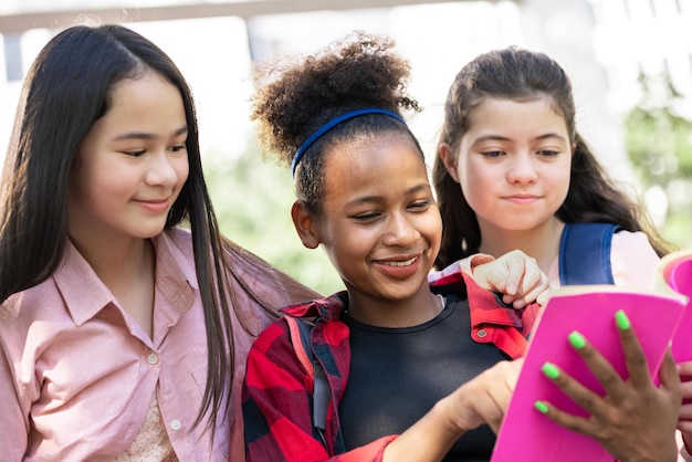 Libro di lettura della ragazza dell'allievo con l'amico al parco della scuola