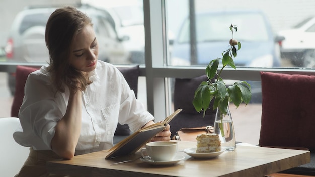 Libro di lettura della ragazza e relax nella caffetteria. ragazza in abiti da lavoro che riposa durante la pausa pranzo.