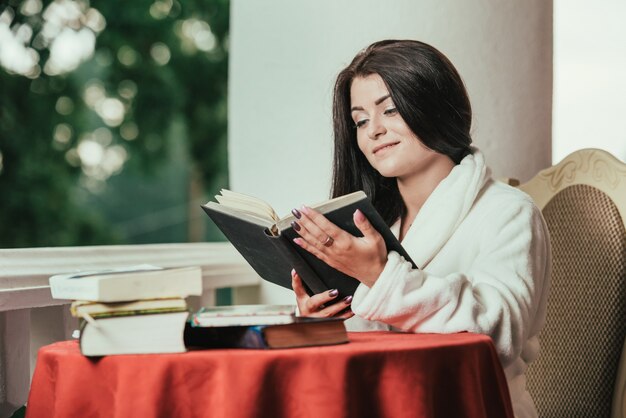 libro di lettura della ragazza mentre bevendo caffè al giorno soleggiato che si siede sul balcone.