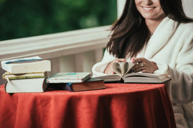 libro di lettura della ragazza mentre bevendo caffè al giorno soleggiato che si siede sul balcone.