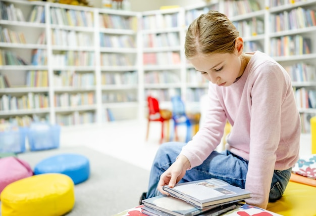 Libro di lettura grazioso del bambino della ragazza in biblioteca