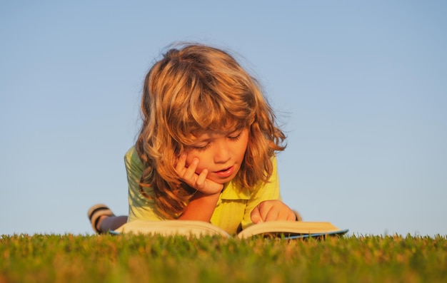 Libro di lettura intelligente del bambino posa sull'erba nel campo sullo sfondo del cielo Ritratto di bambini intelligenti all'aperto