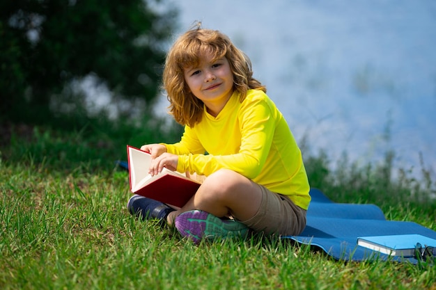 Libro di lettura intelligente del ragazzo del bambino nel parco all'aperto bambino biondo che legge un libro in estate bambini intelligenti all'aperto