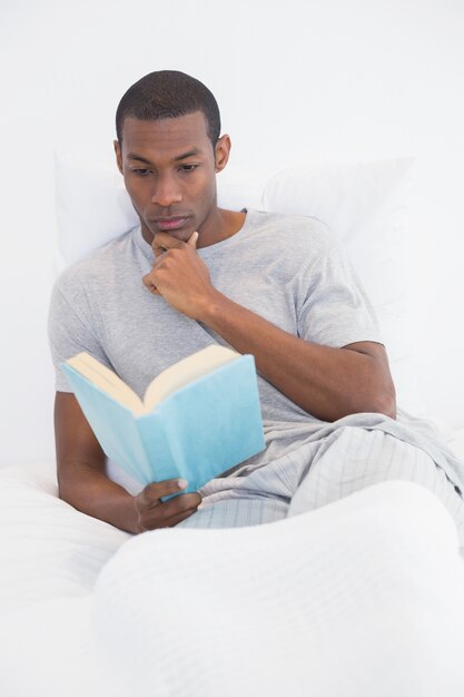 Libro di lettura rilassato dell&#39;uomo di afro a letto