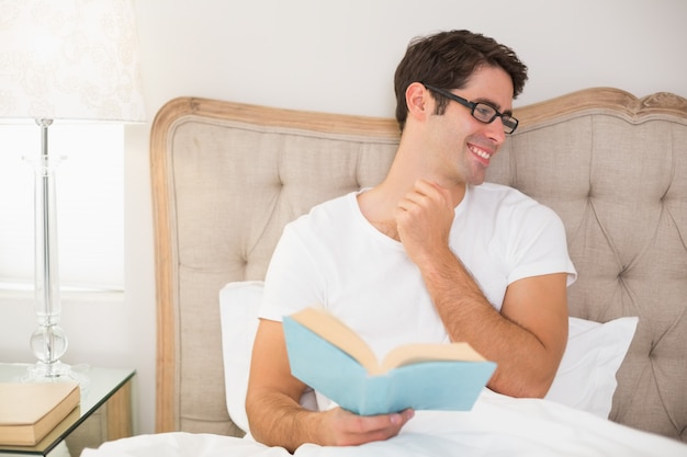 Libro di lettura rilassato sorridente dell&#39;uomo a letto