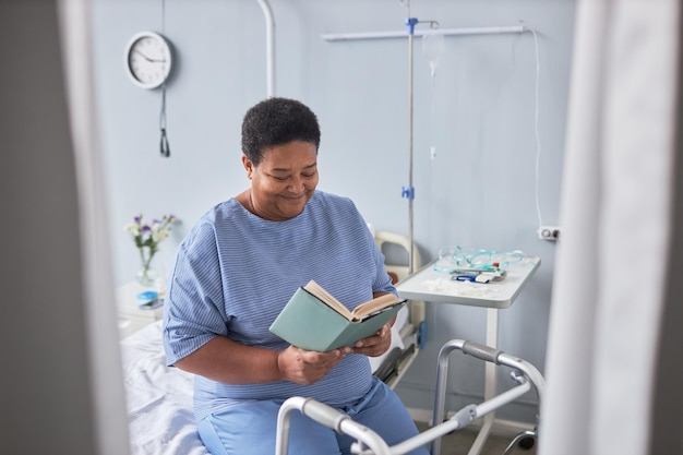 Libro di lettura senior sorridente della donna nella stanza di ospedale