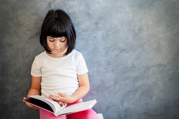 Libro di lettura sveglio della bambina dei capelli neri dalla parete