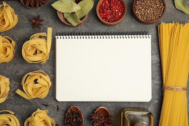 Libro di ricette vuoto spezie e pasta cruda su tavolo grigio scuro piatto Disposizione spazio per il testo