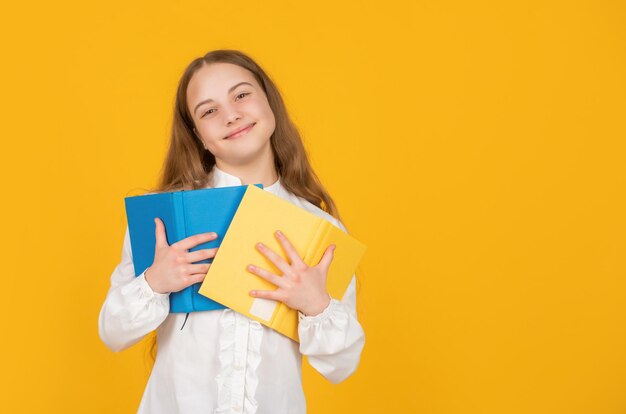 Libro di scuola allegro della tenuta del bambino su fondo giallo con lo spazio della copia, istruzione