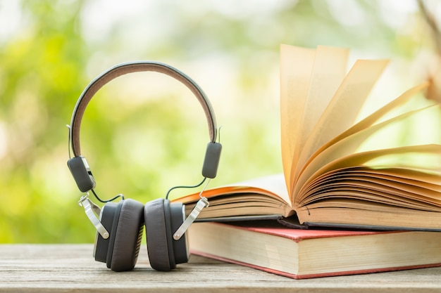 Libro e cuffia nera sulla tavola di legno con la sfuocatura verde astratta della natura. Concetto di lettura ed educazione