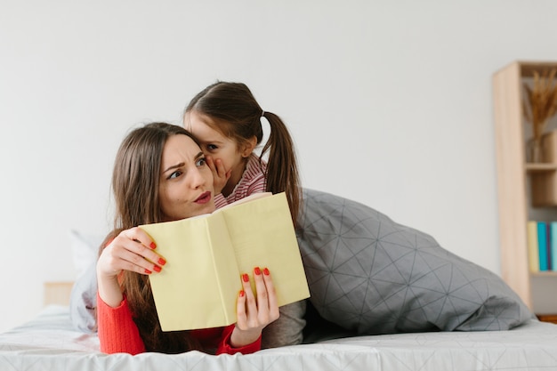 Libro felice della tenuta della lettura della figlia della madre e del bambino della famiglia che si trova a letto