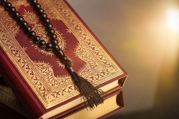 Libro islamico Corano con rosario su sfondo grigio
