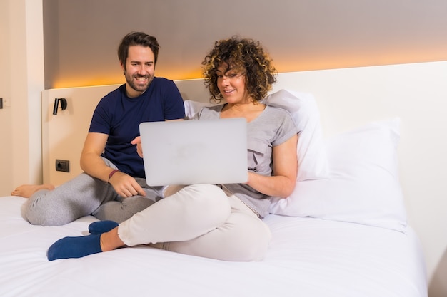 Lifestyle, una coppia eterosessuale caucasica in pigiama sul letto che osserva una prenotazione online sul computer
