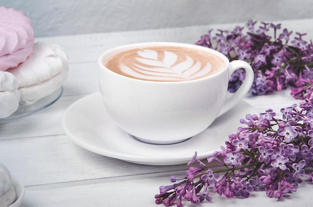 Lillà, tazza di caffè con latte art e marshmallow sul tavolo di legno bianco. Disteso
