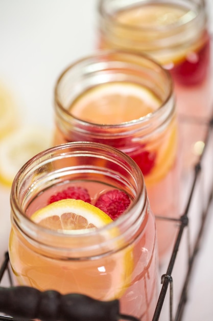 Limonata al lampone in barattoli di vetro da bere su un tavolo bianco.