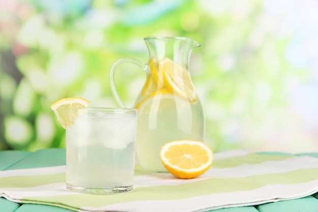 Limonata di agrumi in brocca e bicchieri sulla tavola di legno su sfondo naturale