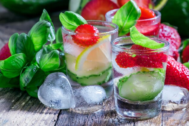 Limonata estiva con ghiaccio alla fragola e limone e foglie di basilico verde vecchio fondo di legno fuoco selettivo