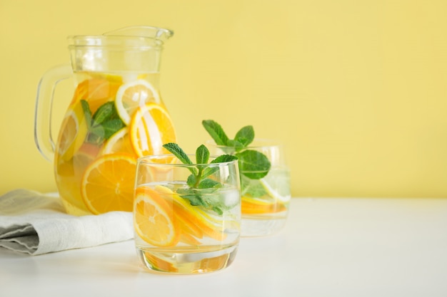 Limonata estiva detox. Acqua con limone, arancia, ghiaccio e menta in bicchiere.