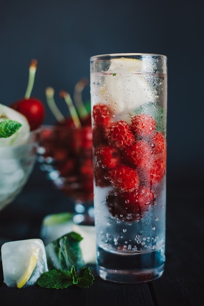 Limonata fredda con lamponi, limone, ghiaccio e ciliegie su sfondo nero