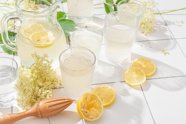 Limonata fresca con limoni e fiori di sago in un barattolo e bicchieri su un tavolo di piastrelle bianche con