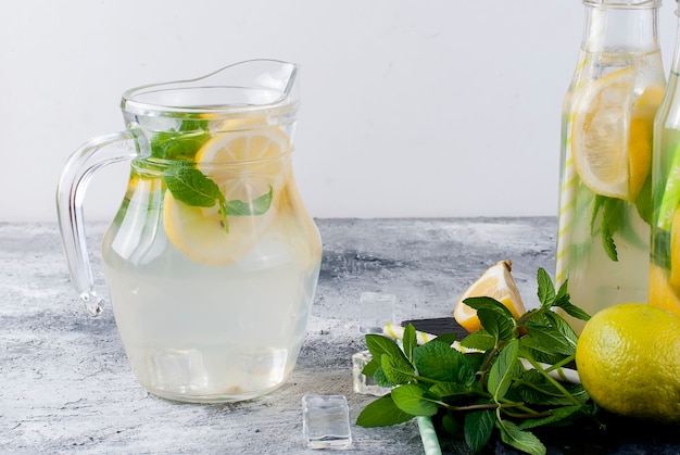 Limonata in caraffa di vetro e bottiglie con ghiaccio e menta