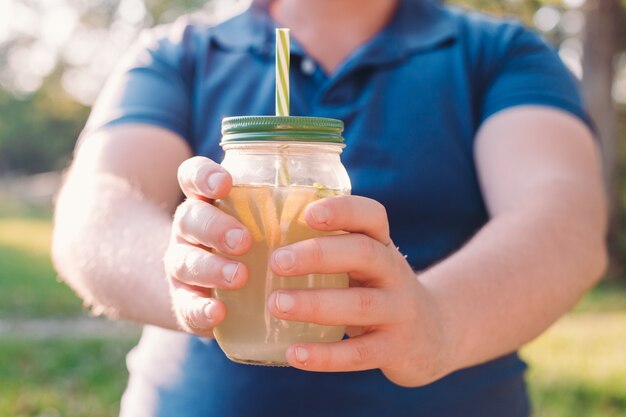 Limonata in mano. Uomo in abbigliamento casual in posa sul parco verde della città in una giornata calda e soleggiata. Vitamine e concetto di vita regolare