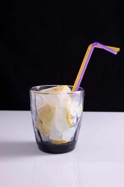 Limonata in un bicchiere con una cannuccia su un tavolo bianco e sfondo nero Minimalista