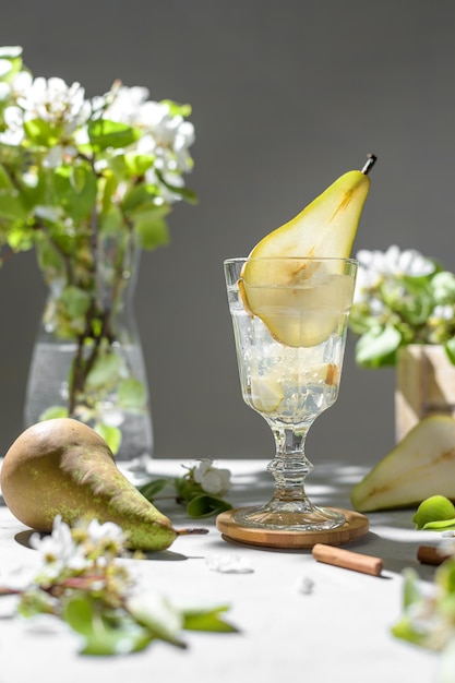 Limonata rinfrescante del cocktail di pere in un bicchiere con purea di pere e frutta fresca e fiori su sfondo grigio chiaro del tavolo