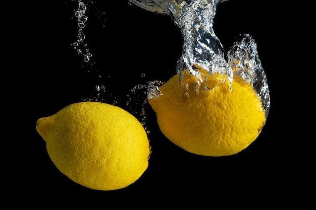 Limone giallo fresco nella spruzzata dell'acqua isolata sul nero.