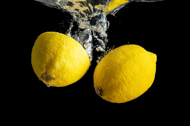 Limone giallo fresco nella spruzzata dell'acqua isolata sul nero.