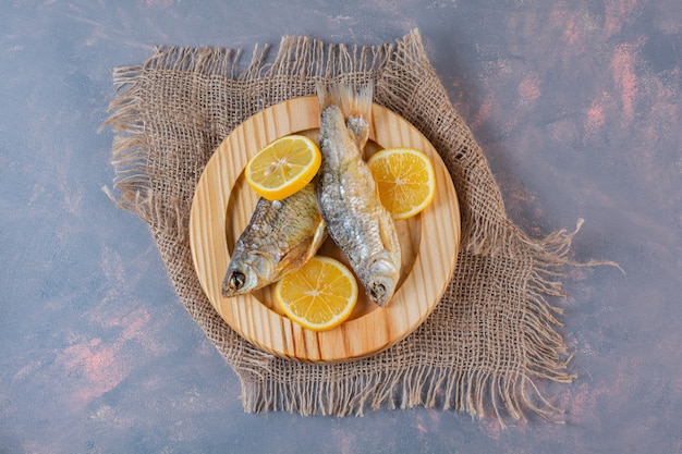 Limoni a fette e pesce salato essiccato su un piatto di legno su un tovagliolo di tela, sulla superficie di marmo