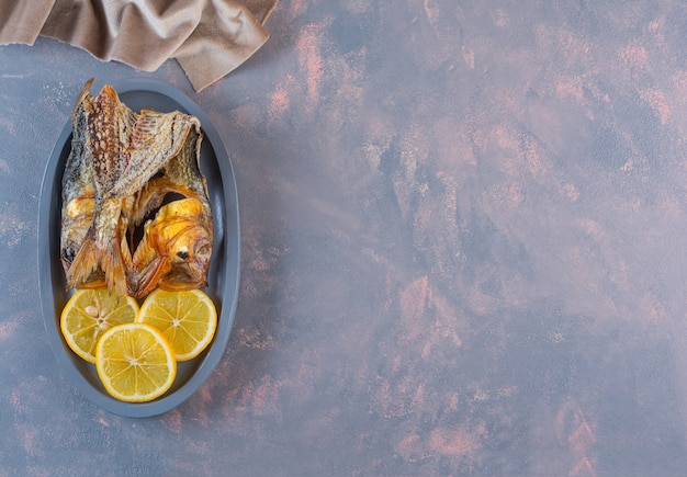 Limoni a fette e pesce salato essiccato su un piatto di legno, sulla superficie di marmo