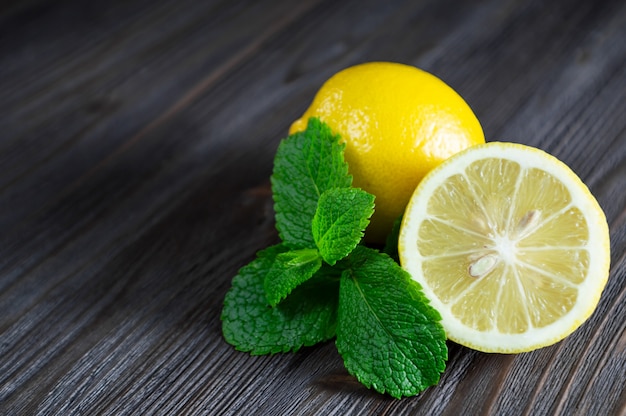 Limoni e foglie di menta freschi sulla tavola di legno scura.