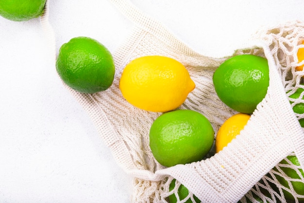 Limoni e lime biologici in un sacchetto a rete riutilizzabile ecologico Zero rifiuti senza plastica e concetto di stile di vita sostenibile Tavolo da cucina bianco sfondo spazio copia vista dall'alto