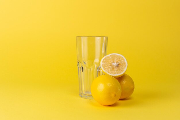 Limoni e tazza di vetro vuota su sfondo giallo