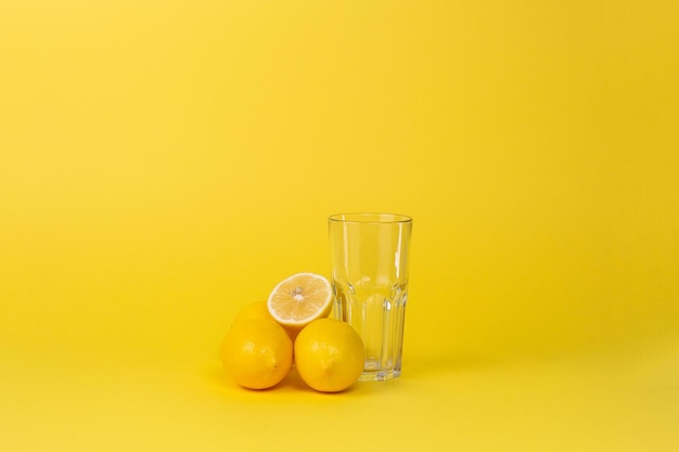 Limoni e tazza di vetro vuota su sfondo giallo