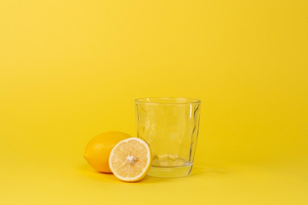 Limoni e tazza di vetro vuota su sfondo giallo